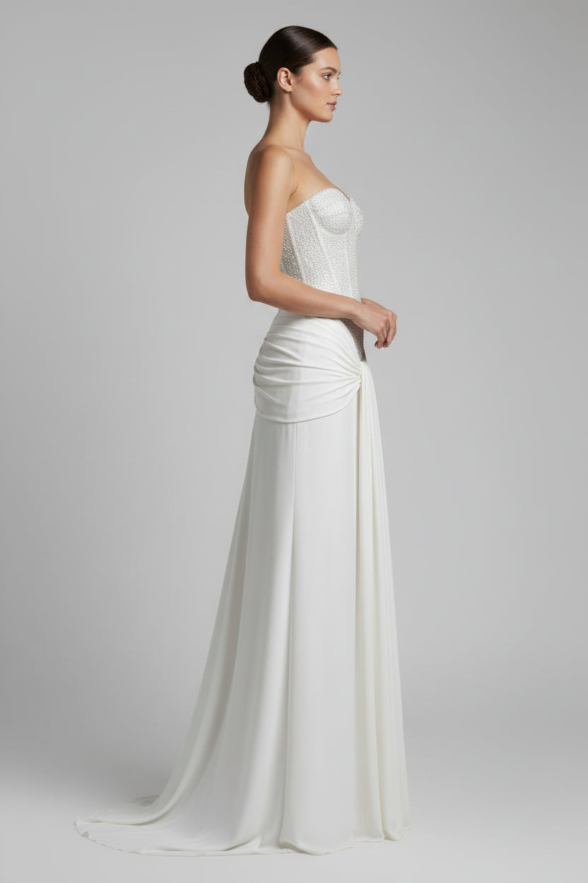 Woman wearing a strapless, embellished wedding gown with a plain background