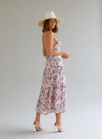 Woman in a floral dress and white hat standing in a modern indoor setting.
