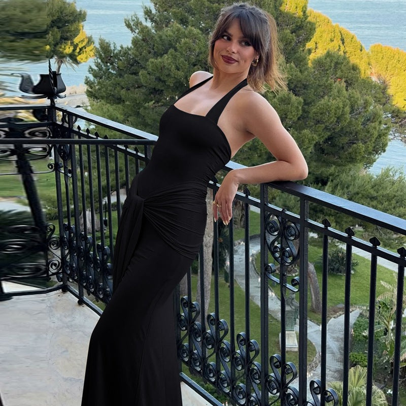 Woman in a black dress standing on a balcony with greenery and water in the background