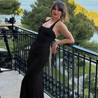Woman in a black dress standing on a balcony with greenery and water in the background