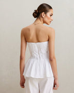 Woman wearing a white strapless top and pants against a plain background