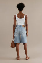 Woman in a white crop top and denim shorts standing in a clothing store.