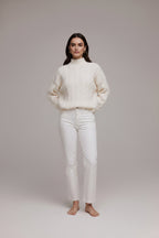 Person wearing a white cable knit sweater sitting on a couch.