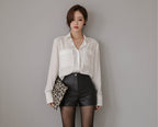 Woman wearing a white blouse and black leather shorts against a brown background