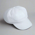 A white, solid-colored, octagonal pumpkin hat made of artificial leather, displayed on a flat surface with printed materials around.