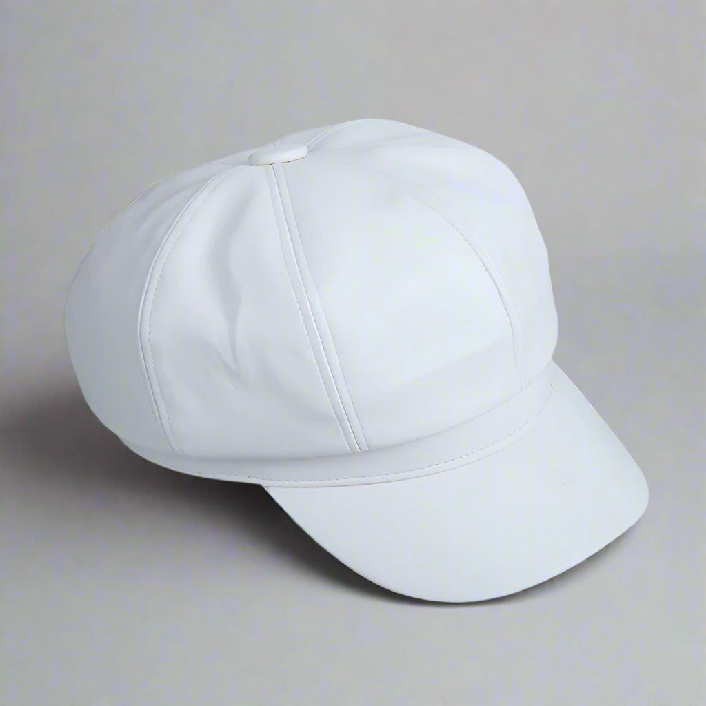 A white, solid-colored, octagonal pumpkin hat made of artificial leather, displayed on a flat surface with printed materials around.