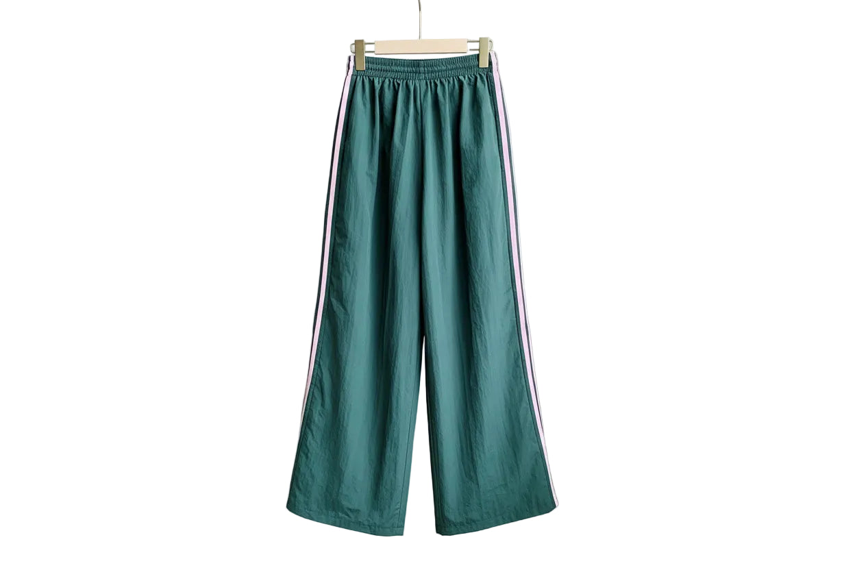 Green pants with pink stripes hanging on a wooden hanger against a neutral wall.