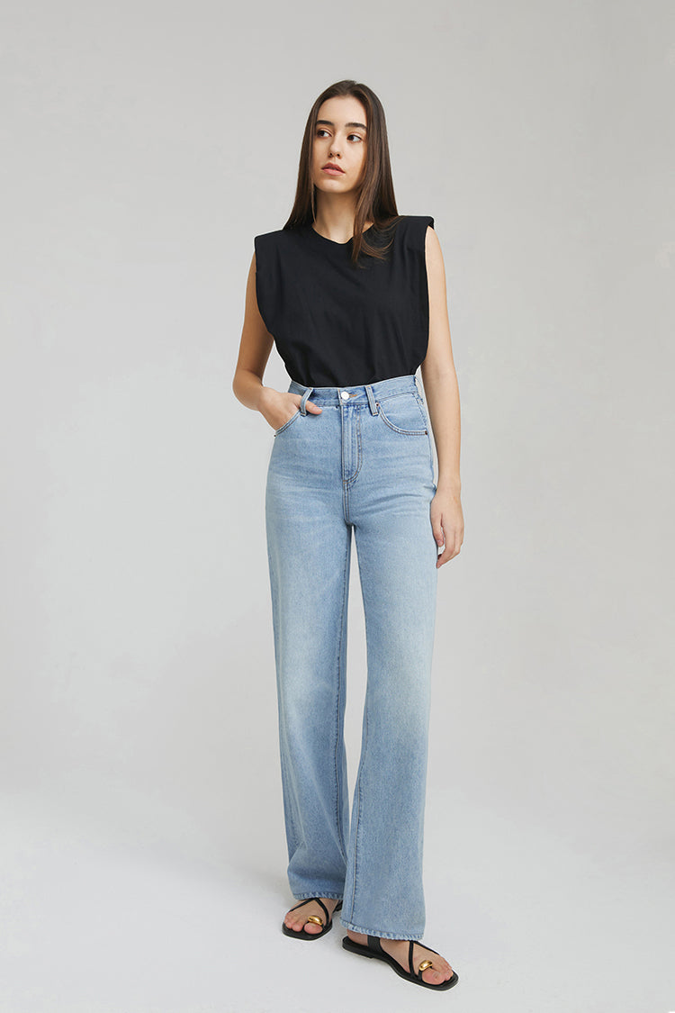 Woman wearing light blue jeans and a black sleeveless top on a gray background