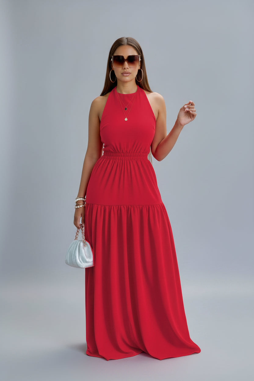 A woman wearing a red sleeveless maxi dress with a halter neckline and a backless element, standing outdoors.