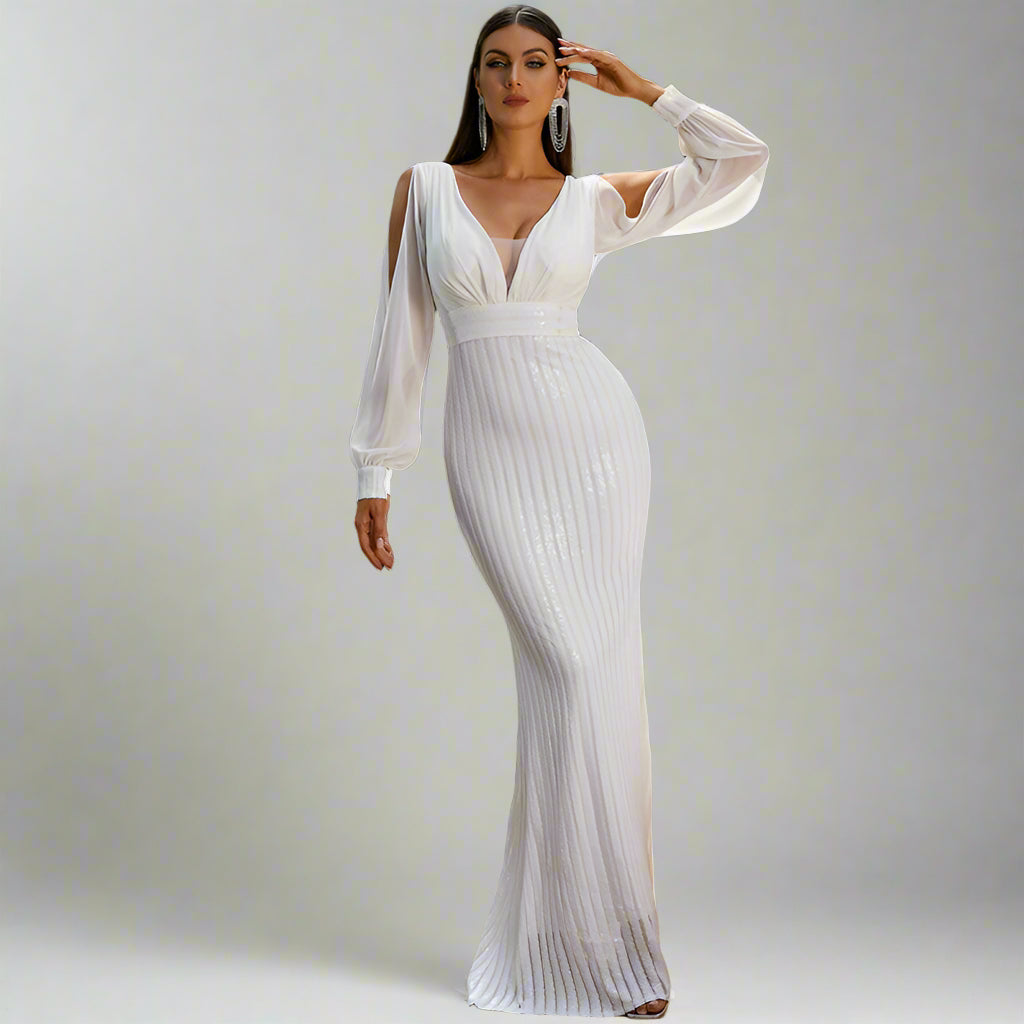 A woman standing on a balcony wearing a white, V-neck, long sleeve evening dress with lantern sleeves, and sequins on the top.